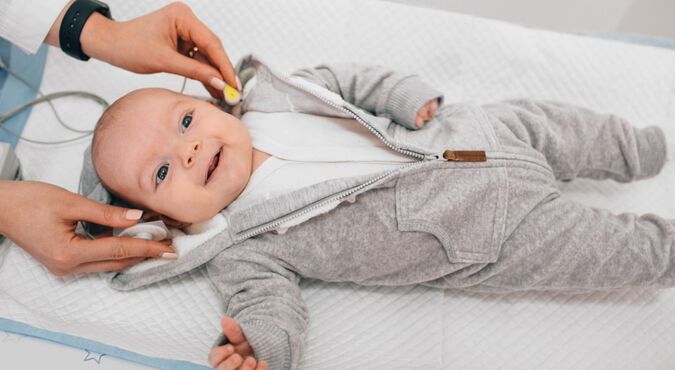 Bebê sorridente realizando teste da orelhinha com ajuda de aparelho auditivo