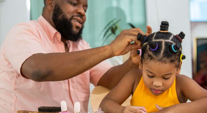 Pai fazendo penteado infantil na filha