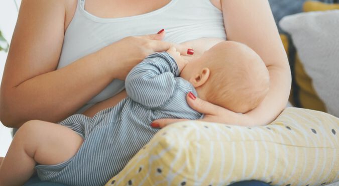 Mãe amamentando bebê posicionado sobre almofada de amamentação