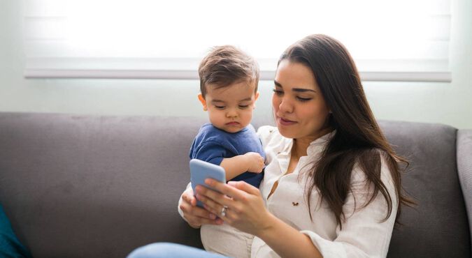 Mãe com bebê no sofá, mostrando smartphone a ele