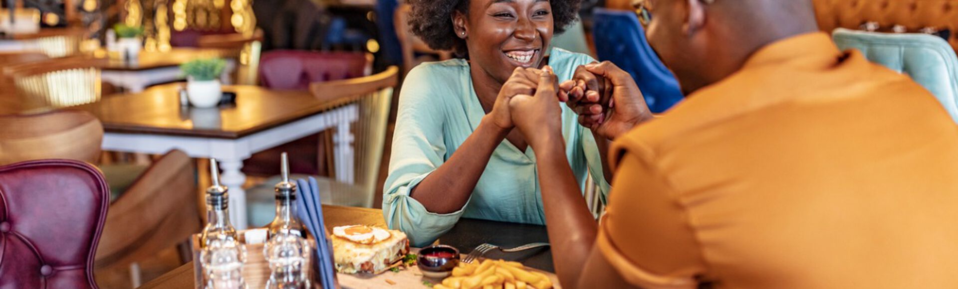 Casal de homem e mulher felizes jantando em restaurante durante vale night para os pais. Ambos são negros e usam roupas claras