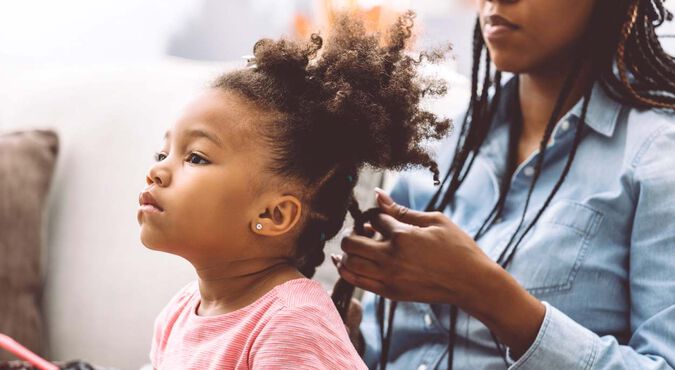 Mãe trançando cabelo crespo da filha na sala de casa