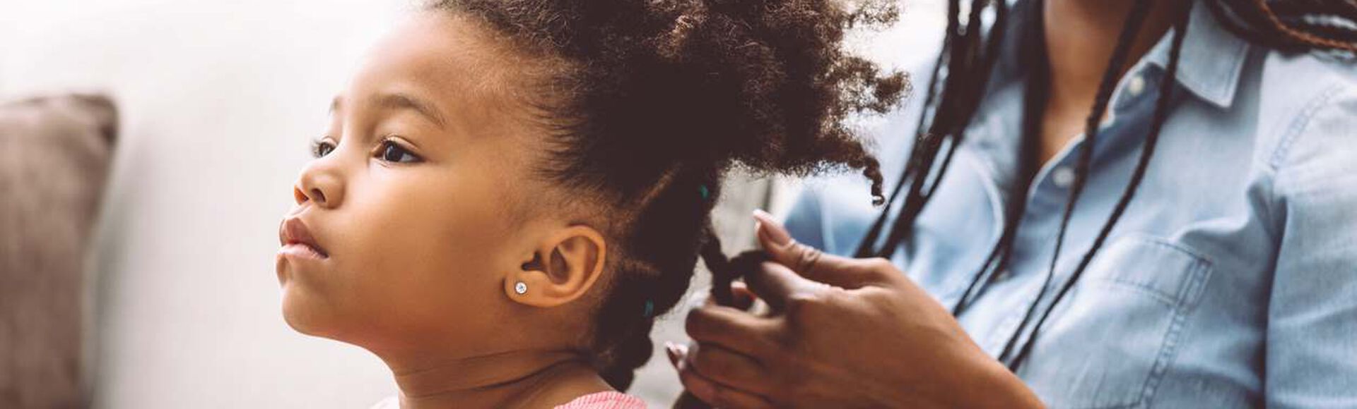 Mãe trançando cabelo crespo da filha na sala de casa