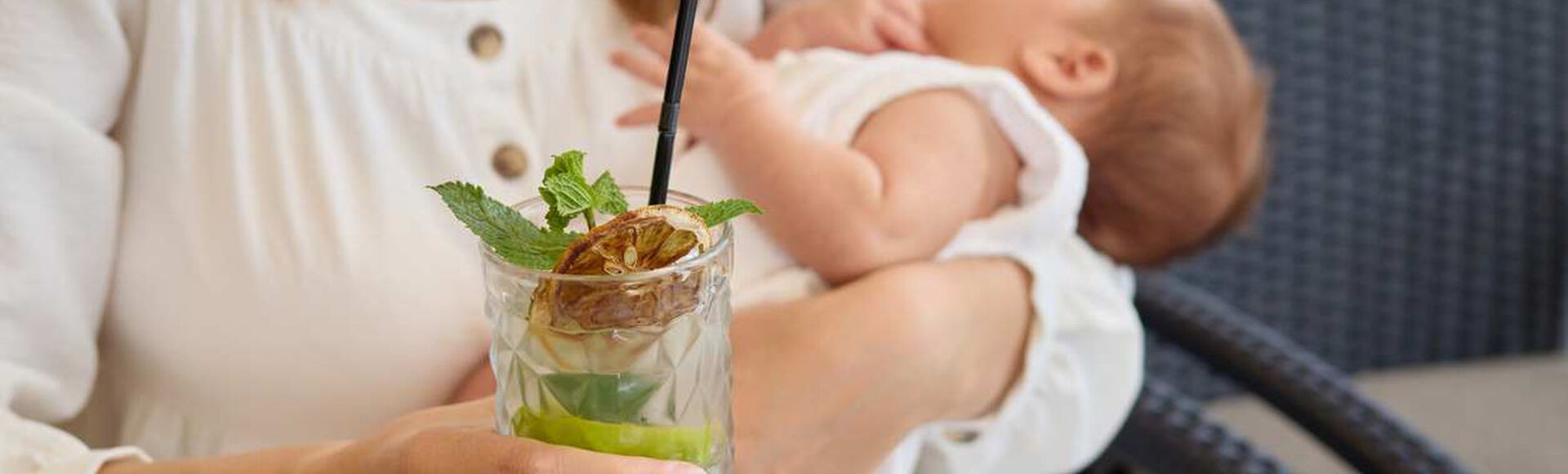 Mãe amamentando bebê enquanto segura um copo com bebida