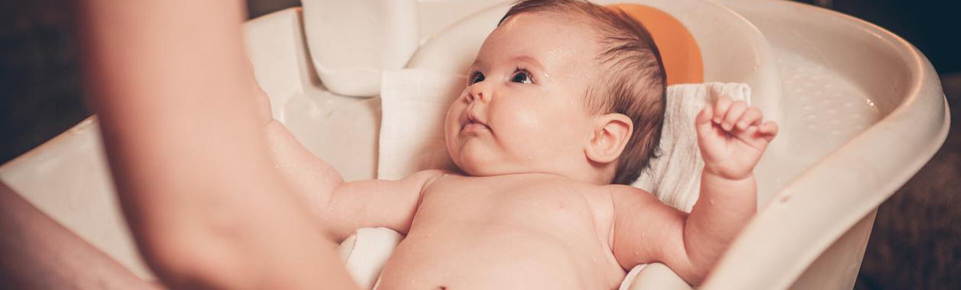 Bebê tomando banho em banheira com atenção voltada para o adulto.