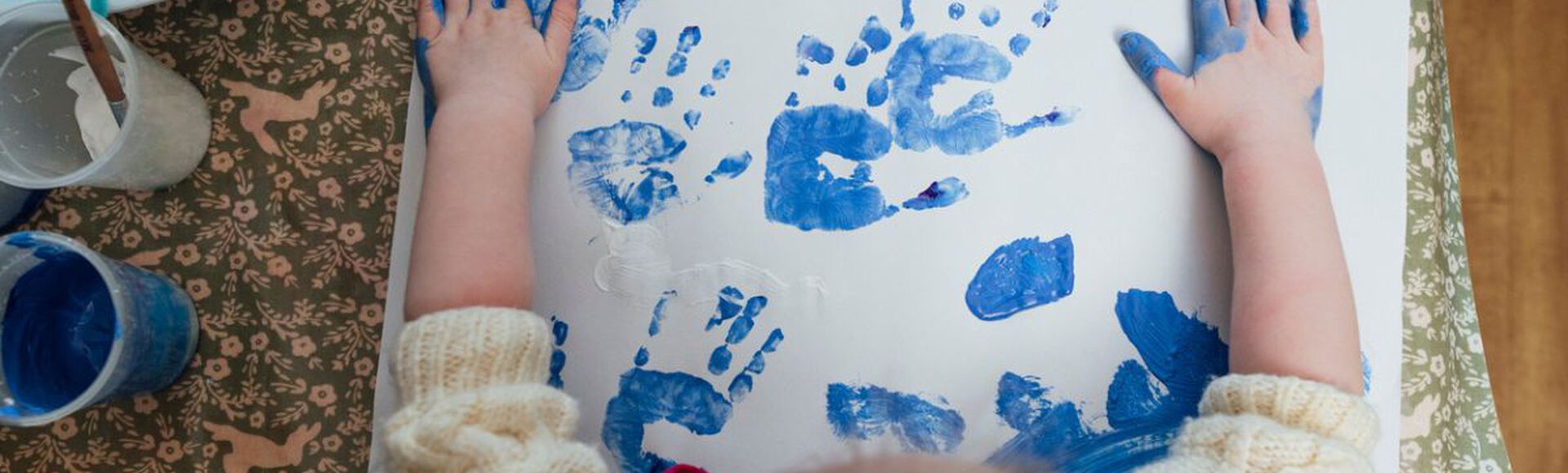 Criança fazendo arte com as mãos, usando tinta azul em uma folha de papel branco.