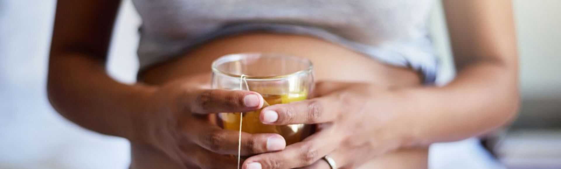 mulher grávida segurando xícara de chá em frente à barriga