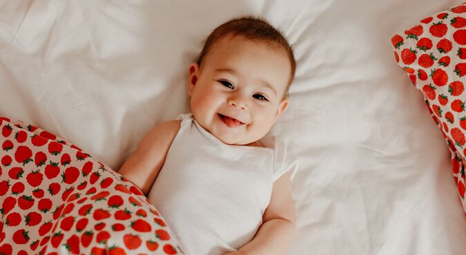 Bebê sorridente deitada e coberta com cobertor com estampa de morangos
