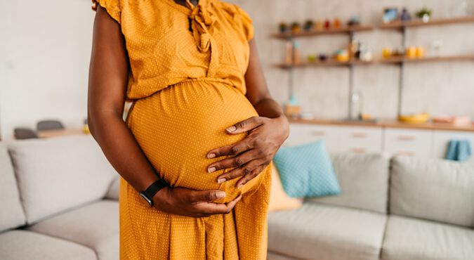 Mulher grávida usando vestido vermelho com as mãos em formato de coração na frente da barriga