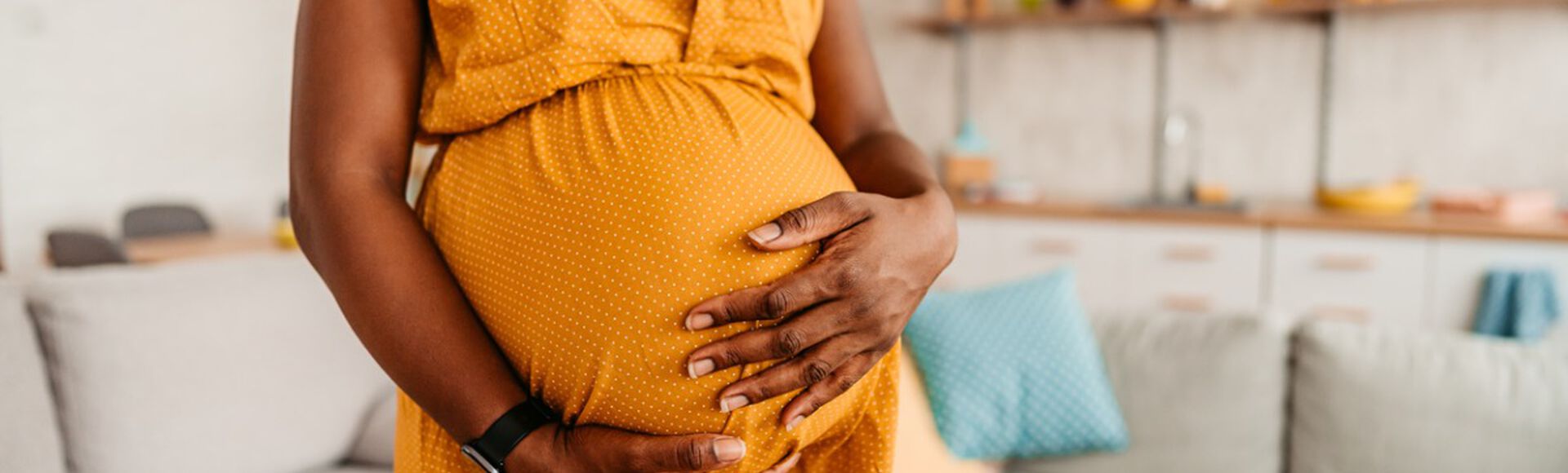 Gestante vestindo vestido amarelo com as mãos na barriga