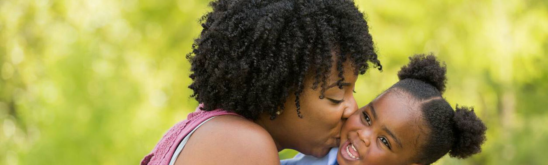 Mãe dando um beijo na bochecha de sua filha, ambas com lindos cabeços crespos.