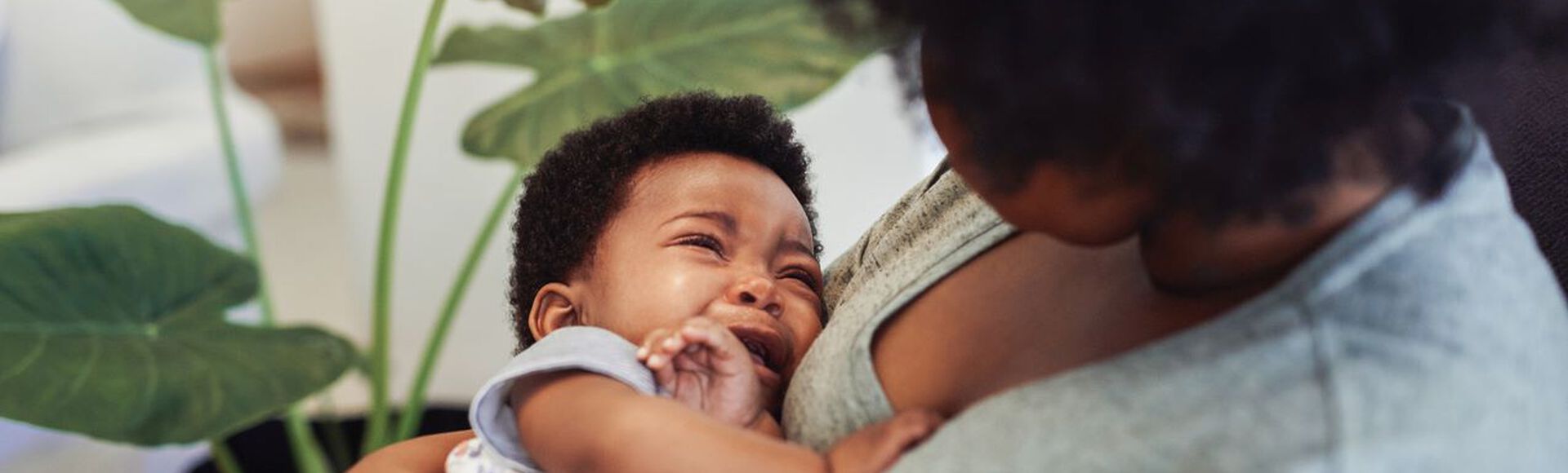 Mamãe consola bebê chorando na hora da bruxa. Não vemos o rosto da mãe que está olhando para o bebê no colo. Os dois são negros.