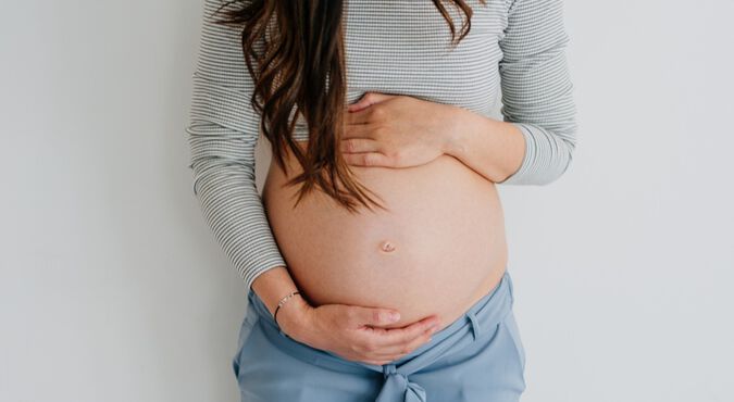 Gestante em pé com barriga à mostra e mãos sobre o abdômen