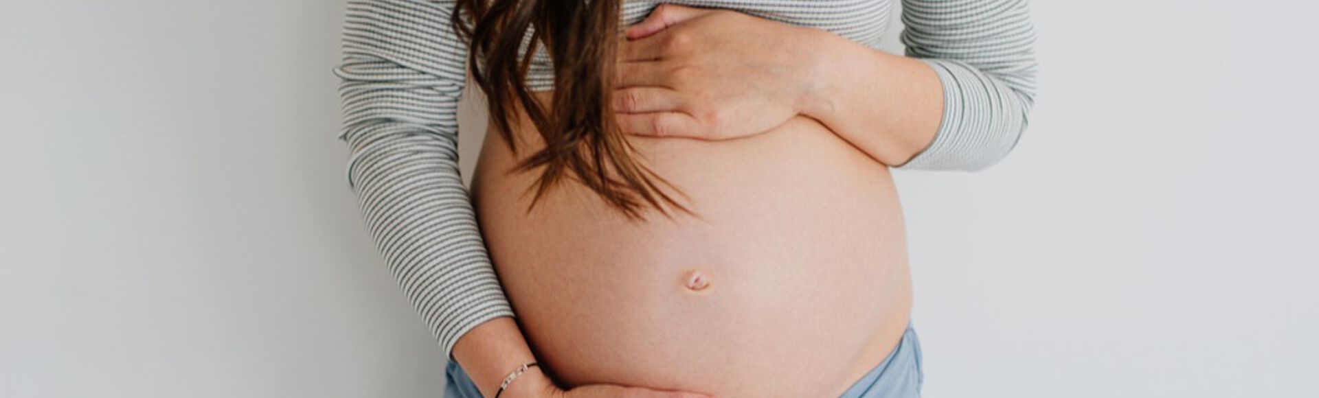 Gestante em pé com barriga à mostra e mãos sobre o abdômen