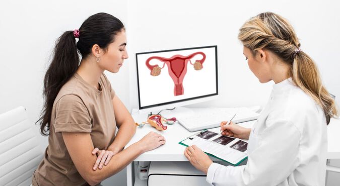 médica explicando um diagnóstico para uma paciente em um consultório. A médica está mostrando um diagrama do sistema reprodutor feminino em um computador