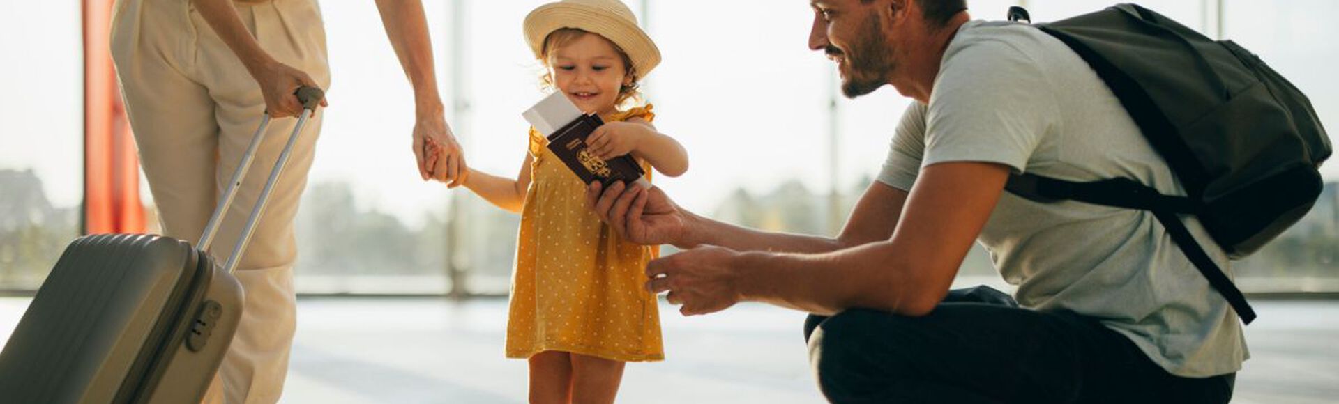 Criança em pé rodeada por pais segurando documentos para viajar em aeroporto