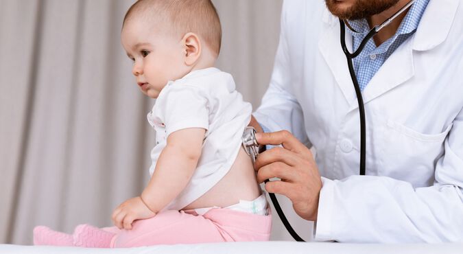 médico usando um estetoscópio para examinar um bebê sentado em uma mesa de exame.