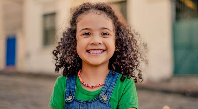 Linda e sorridente menininha com seus cachos bem cuidados.