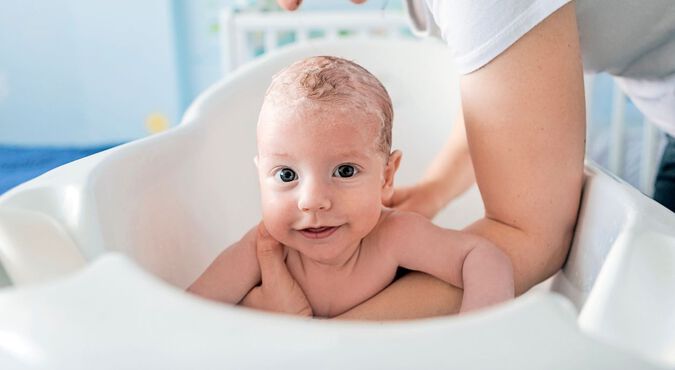 Bebê sorridente tomando banho com o cabelo ensaboado