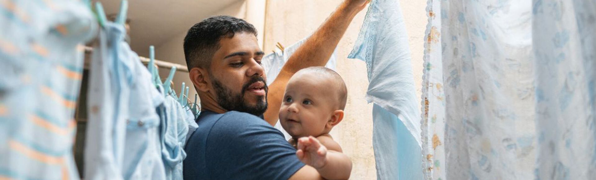 Pai cuidando do filho bebê enquanto pendura roupas no varal