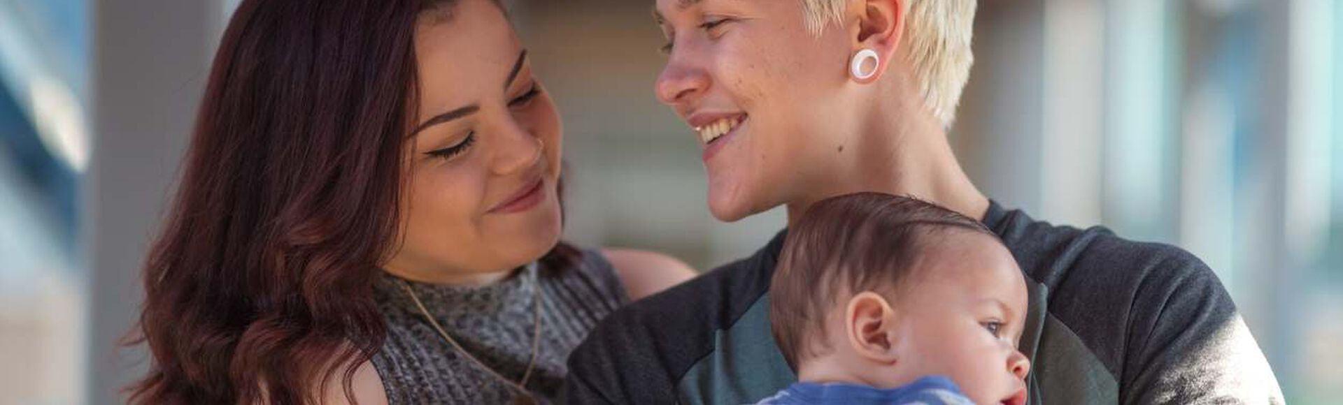 Casal LGBTQIA+ com bebê sorrindo ao ar livre