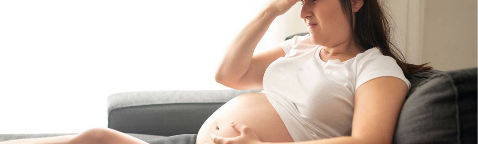 Mulher grávida sentada no sofá com expressão de desconforto