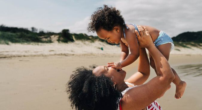 Mãe brincando com seu bebê na praia em um dia ensolarado.