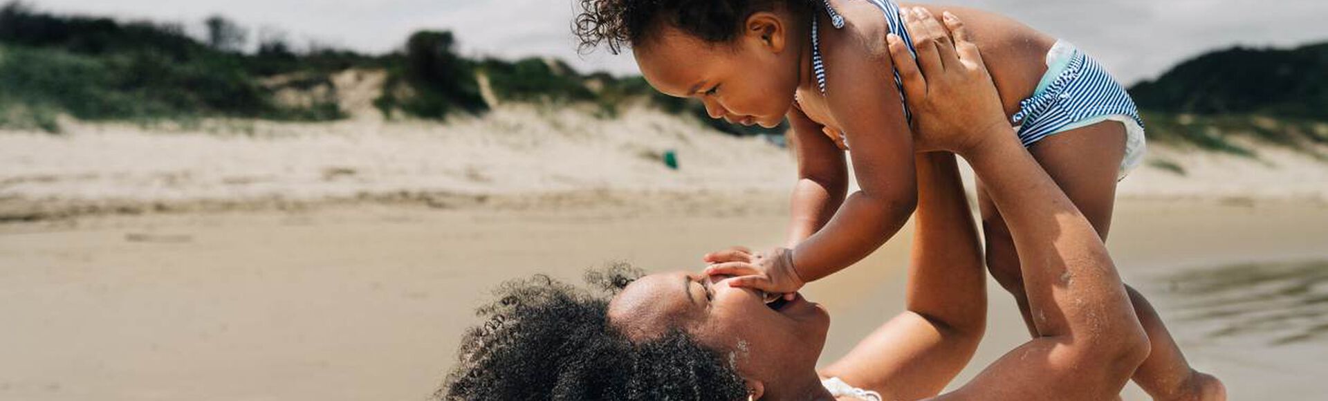 Mãe brincando com seu bebê na praia em um dia ensolarado.