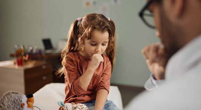 Menina tossindo enquanto conversa com um médico em consultório.