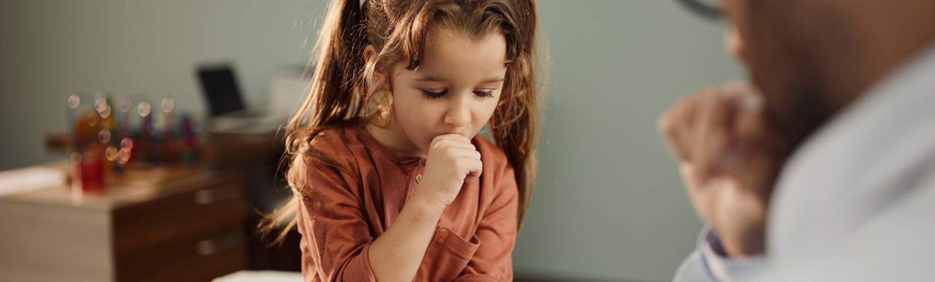 Menina tossindo enquanto conversa com um médico em consultório.