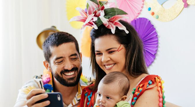 Mãe com o bebê no colo ao lado do pai, fantasiados para o Carnaval, enquanto tiram selfie