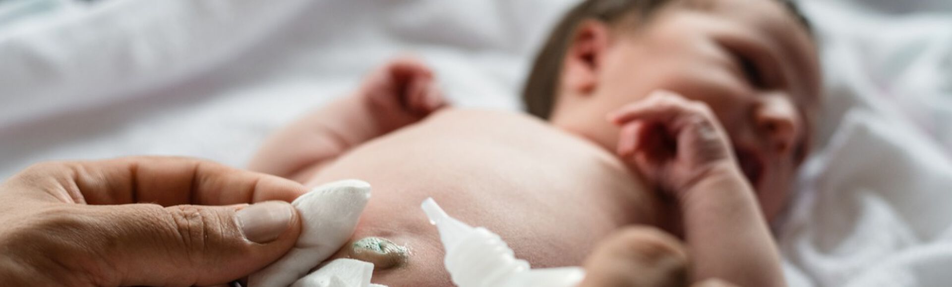 Recém-nascido branco, deitado no trocador, tem resquício de cordão umbilical limpo. Aparece apenas a mão da pessoa que limpa