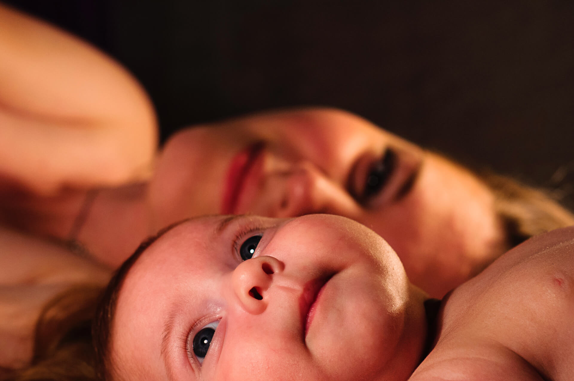 Bebê deitado com a mãe sorrindo ao fundo