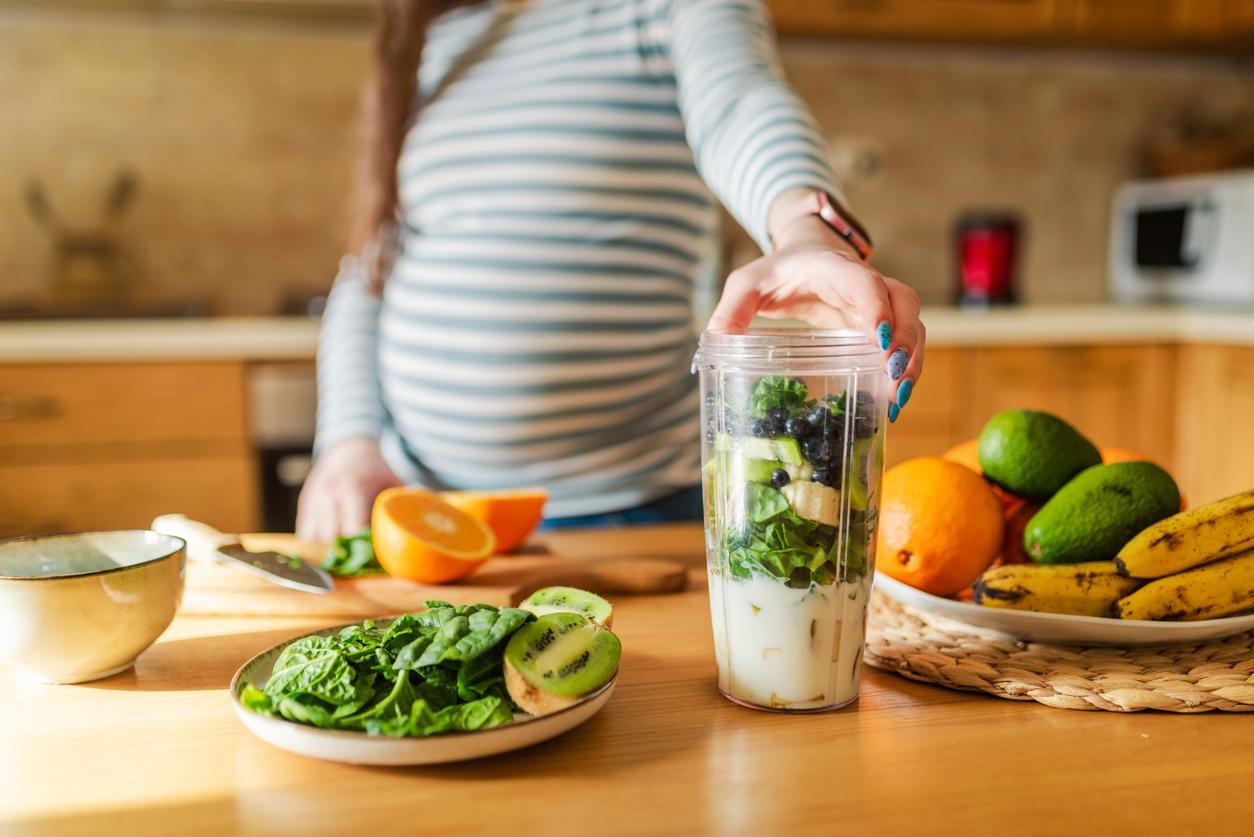 Gestante preparando um shake com folhas e outros alimentos saudáveis.