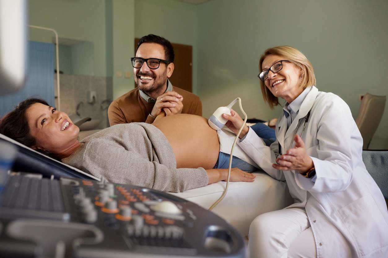 Papai e mamãe de mãos dadas, médica sorridente fazendo ultrassom para verificar se está tudo bem com o bebê.