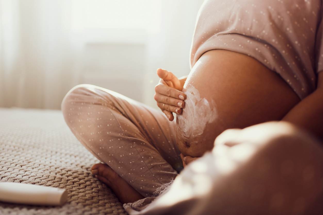 Mulher grávida passando hidratante em sua barriga, sentada no chão da sala