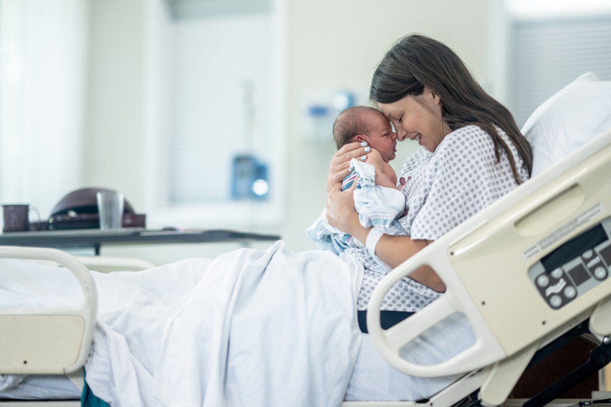 Mãe com bebê recém-nascido no colo em maca de hospital 