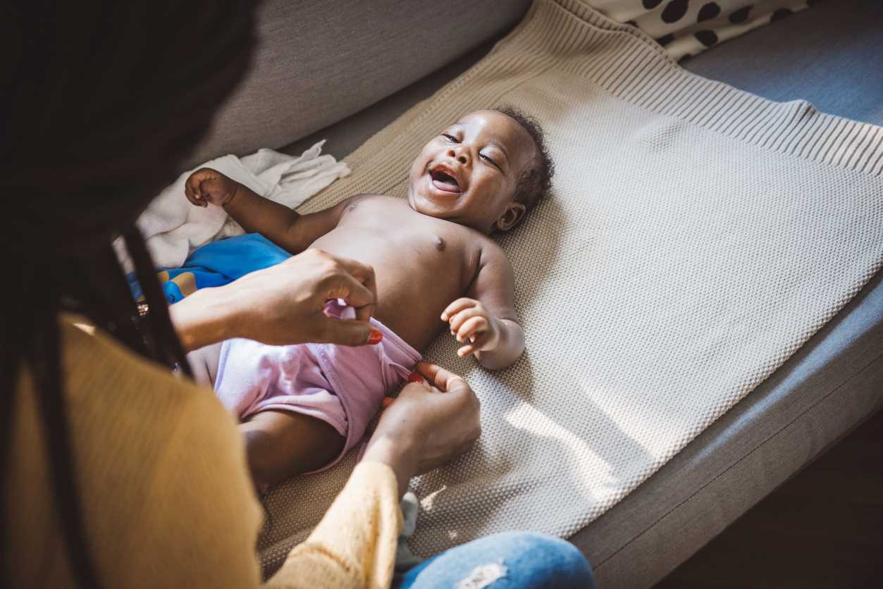 Mãe trocando a fralda de um bebê sorridente.