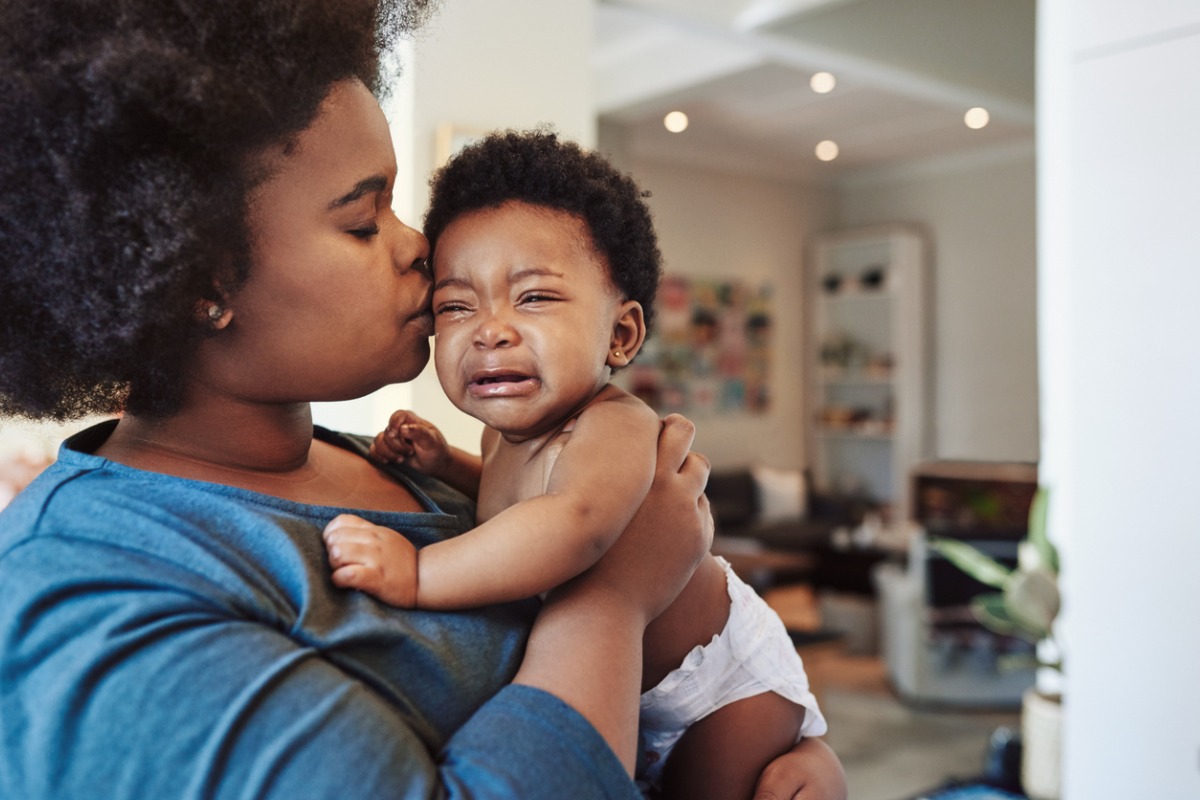 Mãe beija e consola bebê de colo que chora por desconforto causado pela infecção urinária infantil. 