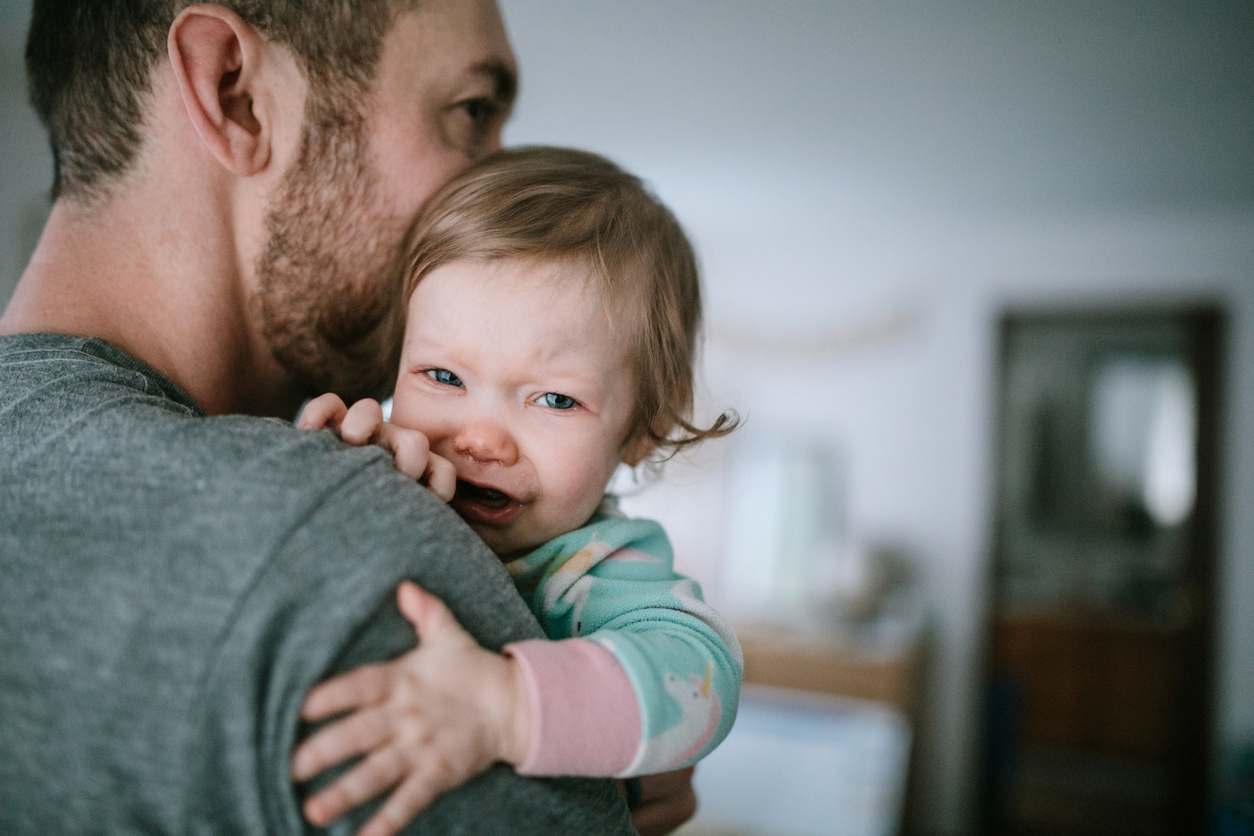 Bebê gripado no colo do pai com expressão de incômodo