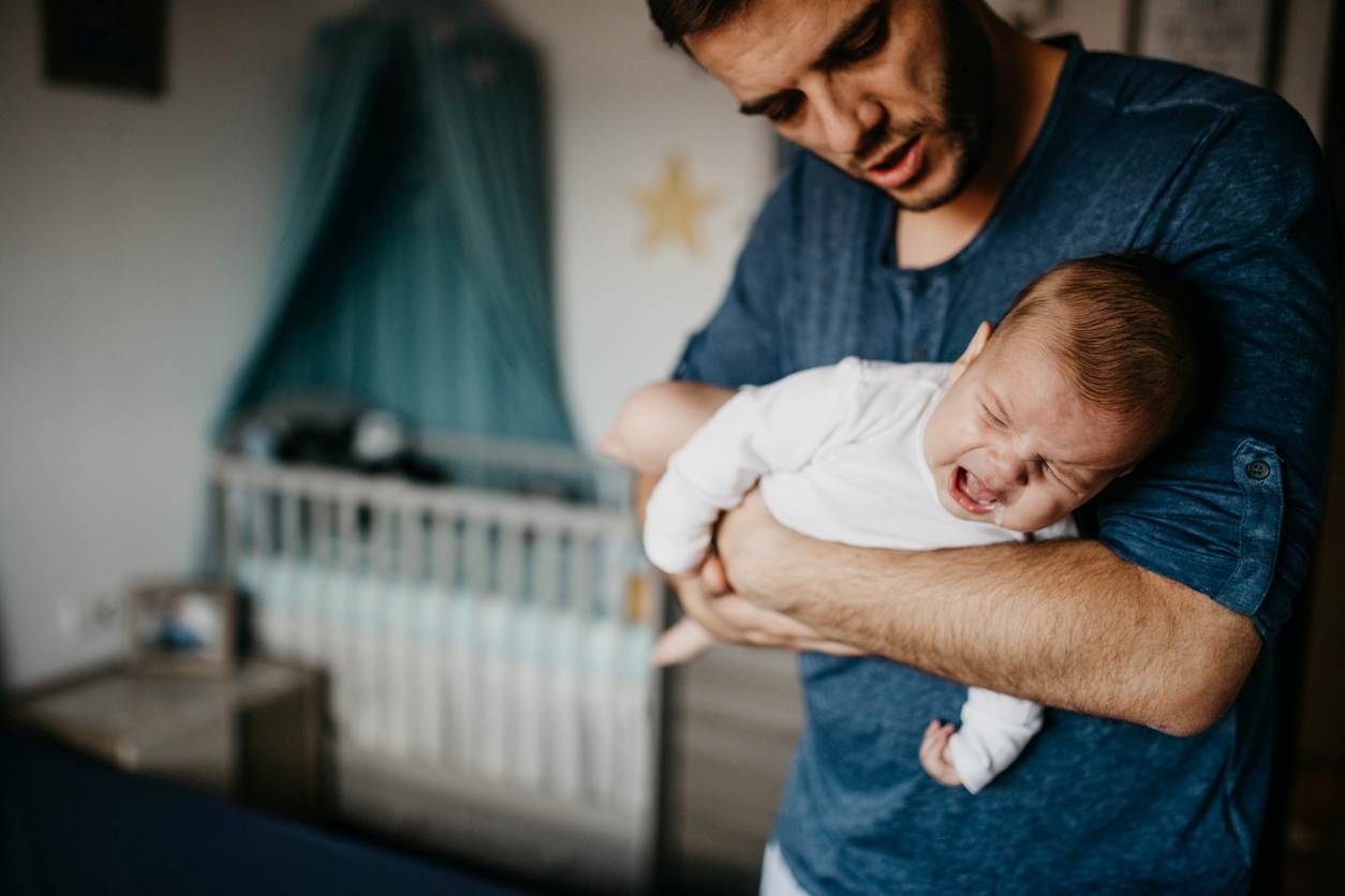 Pai está ajudando seu bebê, que está sofrendo com cólicas noturnas.
