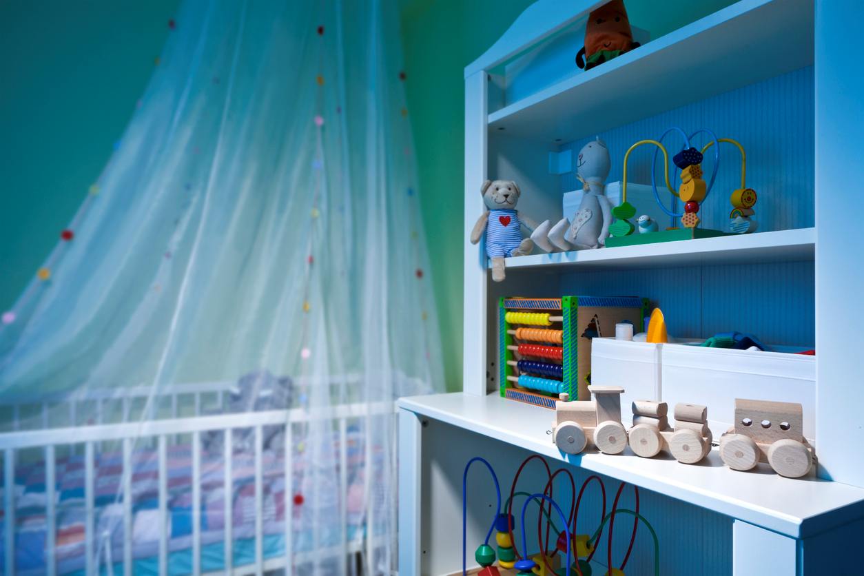 Quarto de bebê em tons claros, decorado com brinquedos de madeira, com berço coberto por mosquiteiro.