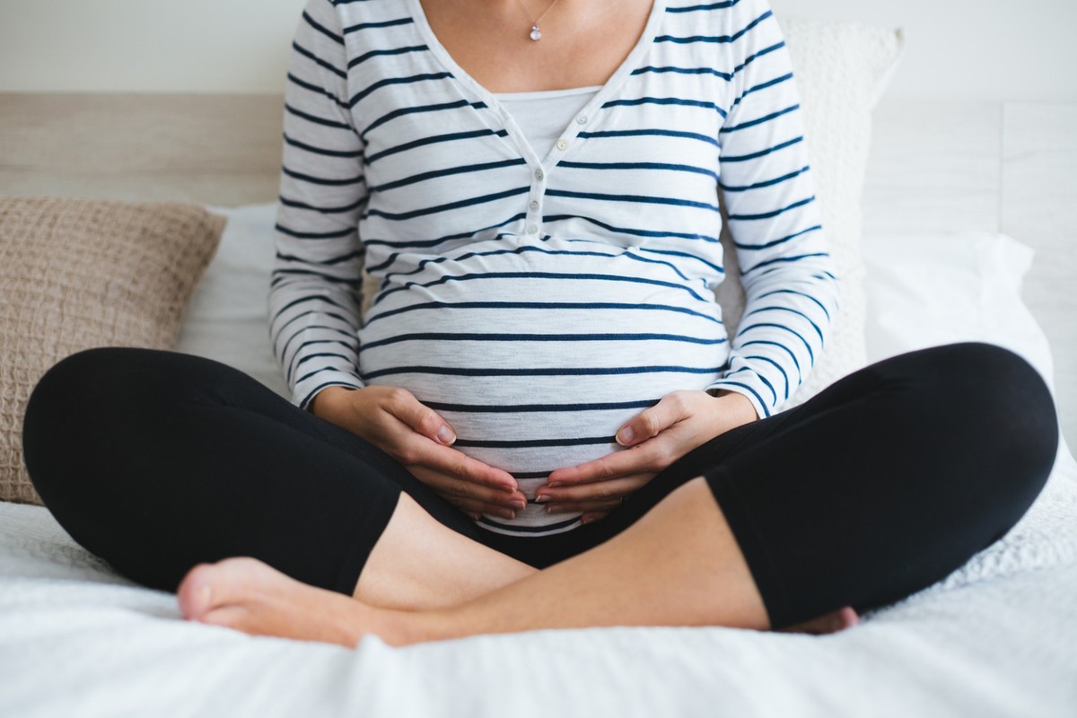 Gestante sentada com pernas cruzadas em frente ao corpo e barriga em evidência