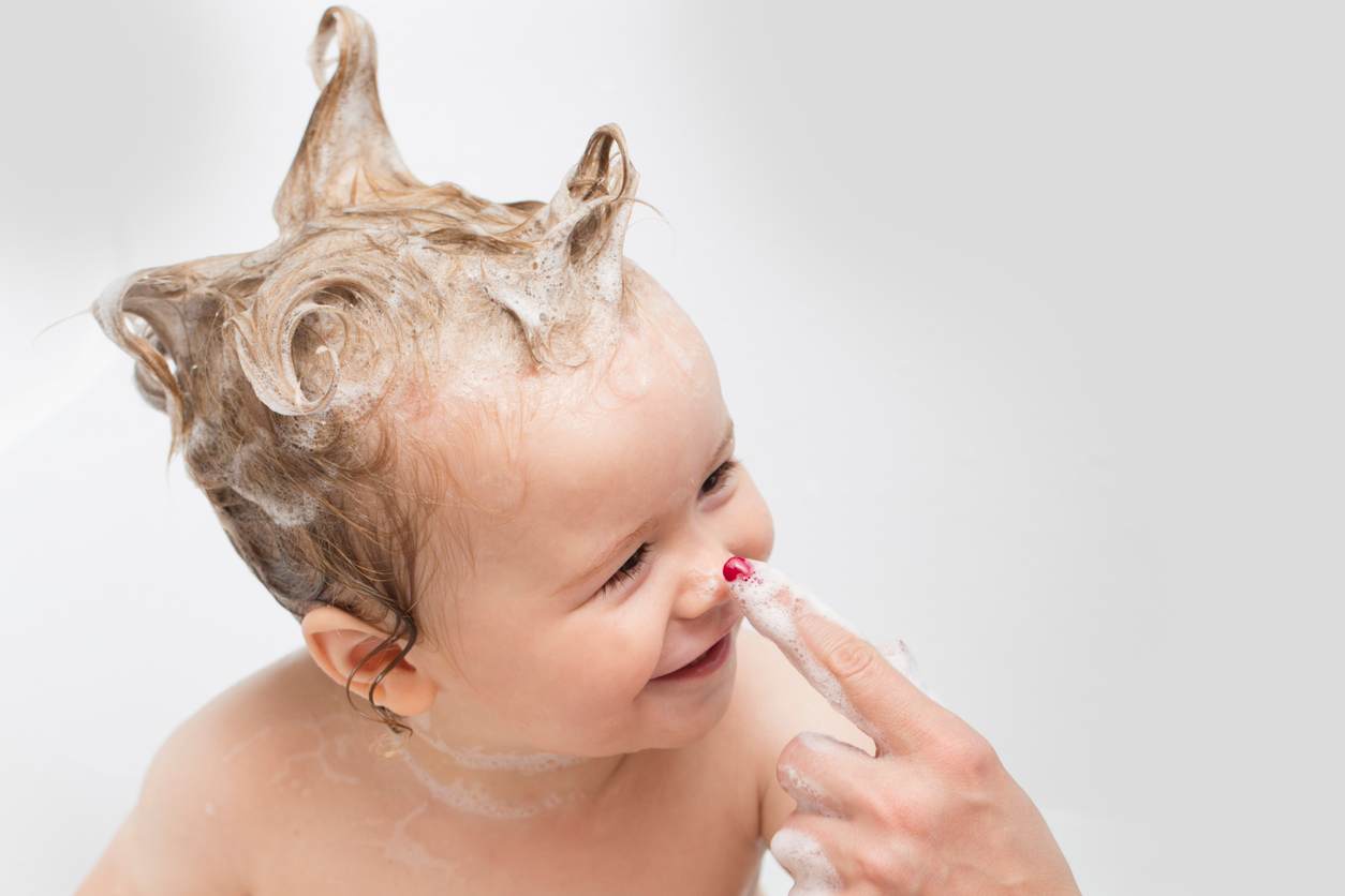 Bebê sorrindo durante o banho com espuma no cabelo 