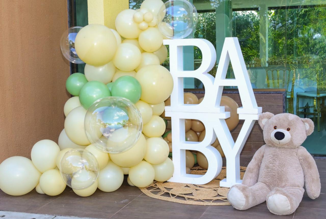 Entrada de festa com decoração para chá revelação. Balões amarelos, verdes e urso de pelúcia gigante com a palavra "baby" 