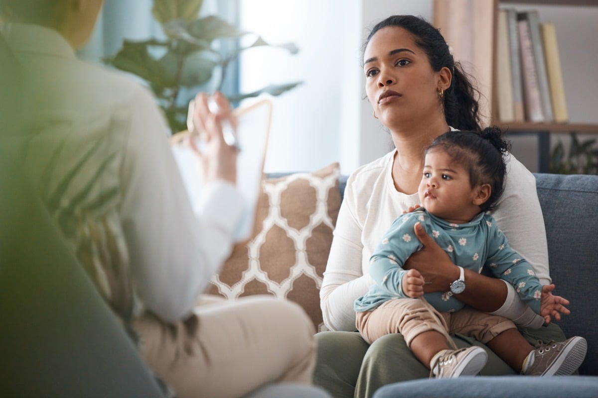 Mãe séria com bebê no colo enquanto conversa com especialista sobre sinais de autismo em bebês. Mãe e filha são mestiças