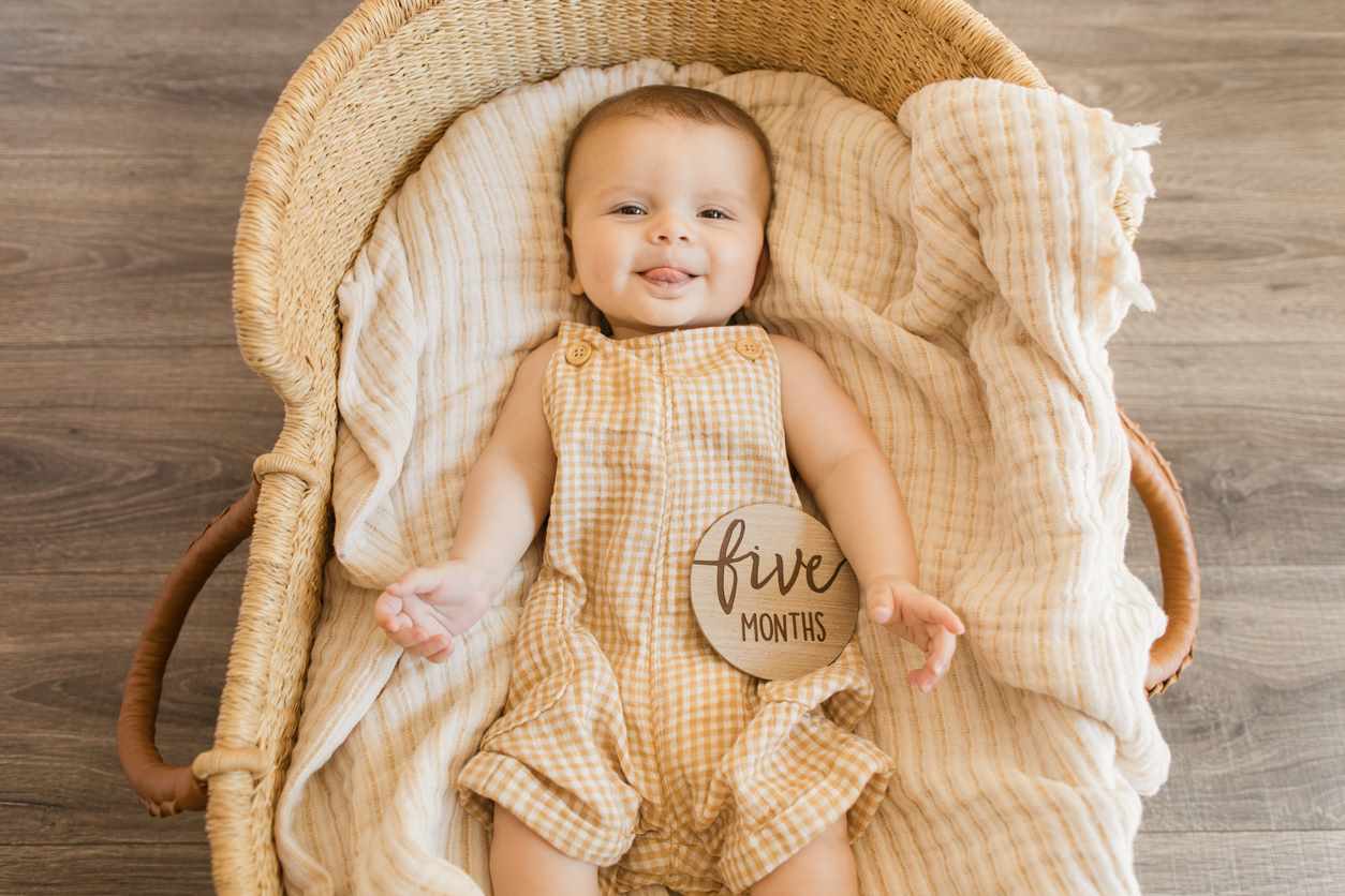 Bebê de cinco meses sorrindo deitado em um cesto acolchoado