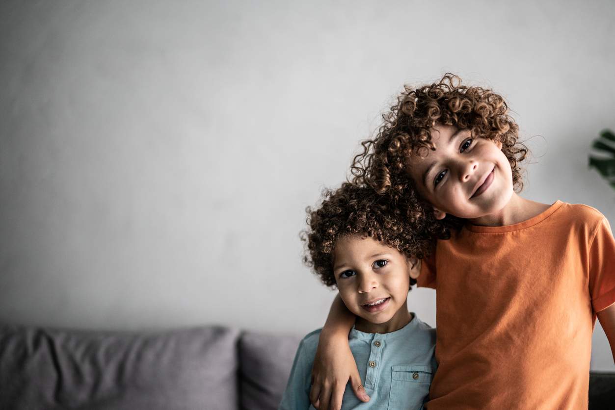 Dois garotinhos de cabelo cacheado, abraçados e posando para a foto.