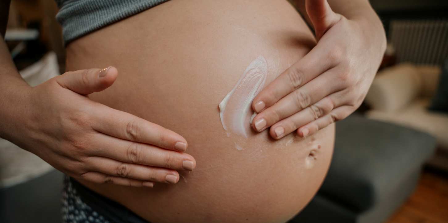 Gestante massageando sua barriga com hidratante à base de óleo de amêndoas.