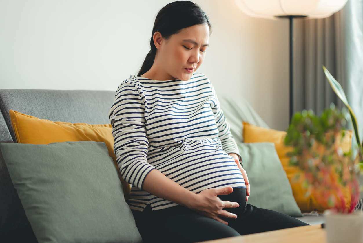 mulher grávida sentada com expressão de desconforto na barriga
